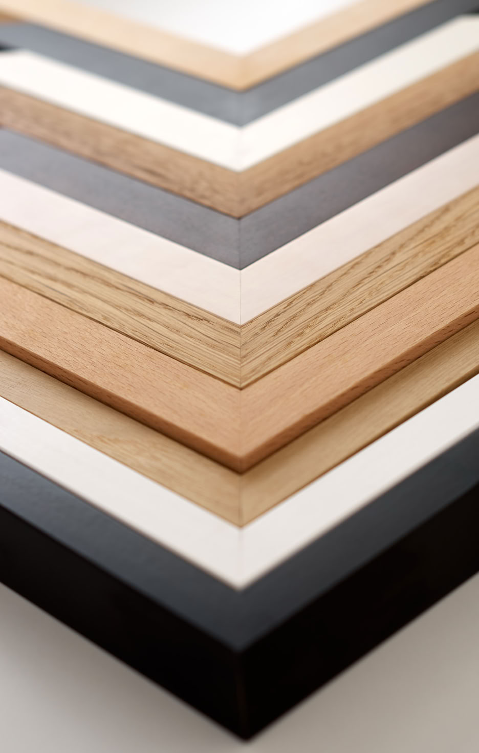 Mehrere hintereinander gelegte Holz-Bilderrahmen-Winkel in verschiedenen Farben und Holzarten.