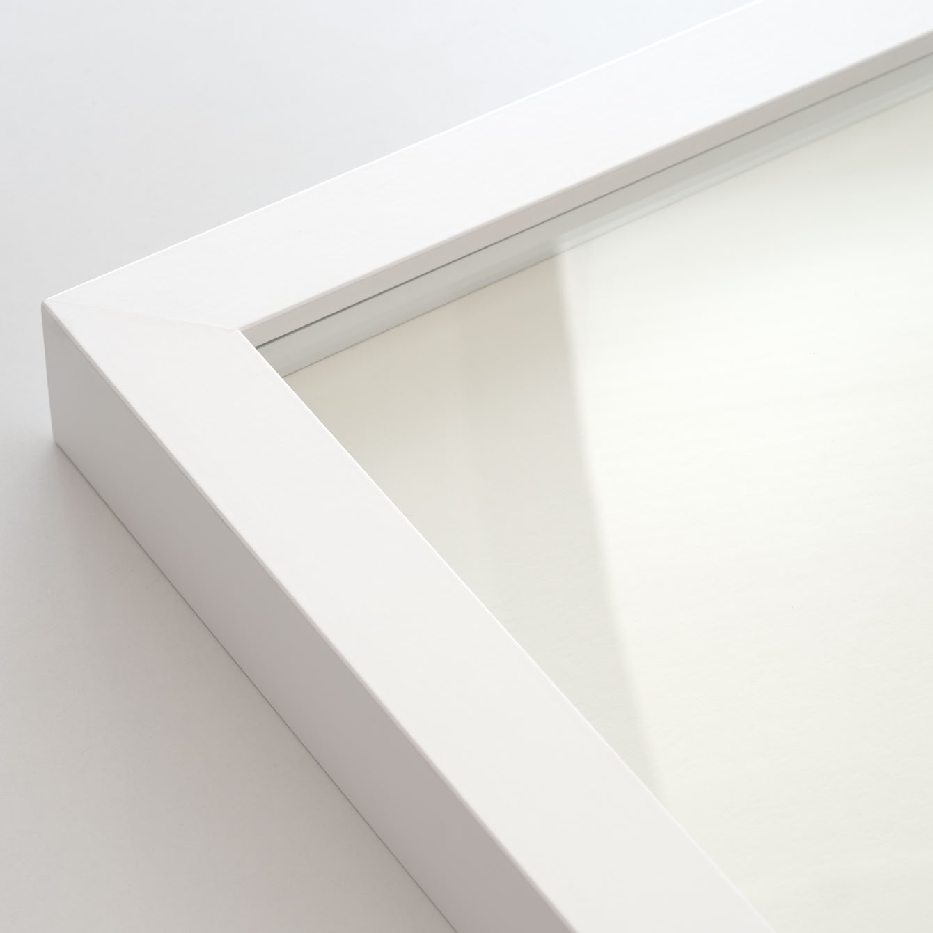 Ecke eines weißen Bilderrahmens mit Normalglas-Scheibe.
