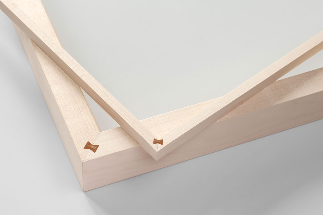 Zwei überlappende Bestandteile eines Holzrahmens, auf einer hellgrauen Oberfläche liegend.